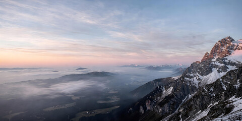 Breathtaking view from mountain top of cloud-filled valley at dawn or dusk, illuminated by soft, pastel colors.