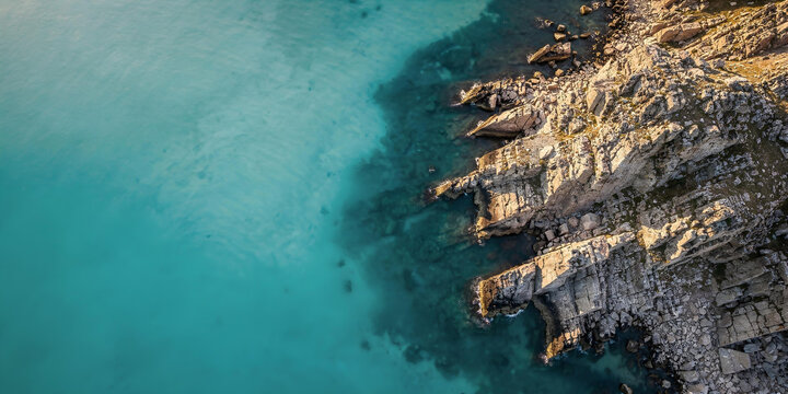 Aerial view of a rocky coastline abruptly meeting clear turquoise or blue sea water.