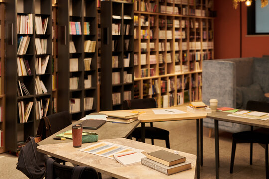 Empty library interior showing bookshelves filled with books, several tables with open notebooks arranged for study session