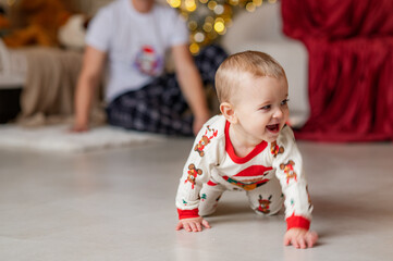 A one-year-old baby crawls on all fours, dressed in a New Year's outfit, crawling around a New Year's-decorated room, smiling. New Year and Christmas. Parenting. Family
