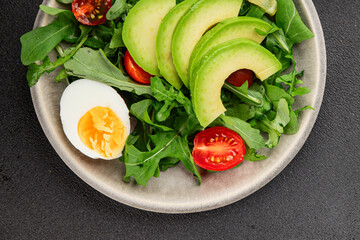 Avocado salad arugula, egg, tomato, mixed greens, vegetables dish fresh delicious gourmet food background tabletop rustic food top view copy space keto and paleo diet vegetarian food