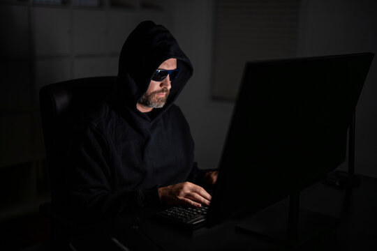 Cyber criminal and stolen personal data. Digital thief. Hacker programmer in hoodie at office laptop, gaming. Hacker attack. Hacker gamer at night in office. Cyber attack. System breach