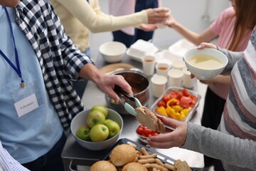 Volunteers giving food to homeless people in shelter, closeup