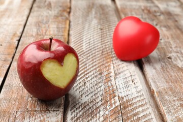 Ripe apple with carved heart and heart model on color wooden table, closeup