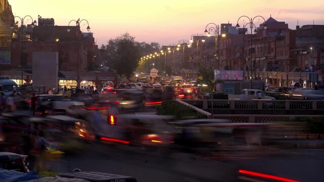 A day to night time-lapse wide shot of a busy or congested city crossroad with street lights turning on, clouds disappearing into darkness, and moving traffic of vehicles on an Indian road