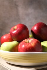 Fresh red and green apples in bowl on wooden table against grey background, closeup