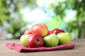 Fresh red and green apples on wooden table against blurred green background, closeup