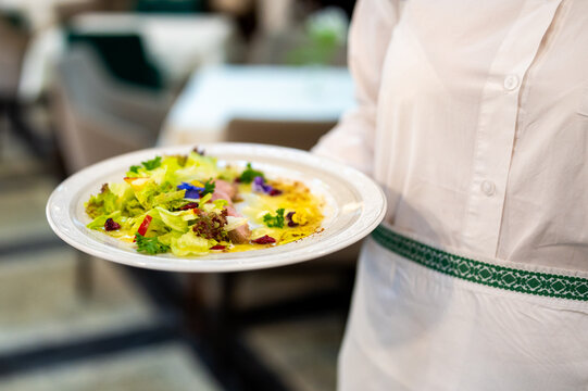 A waiter serves a vibrant, gourmet salad on a white plate in a restaurant setting - Powered by Adobe