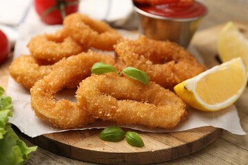 Deep fried squid rings with lemon slice, basil and ketchup on wooden table, closeup