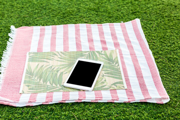 Tablet on a colorful beach towel placed on green grass in a sunny outdoor setting