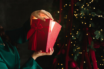 Naklejka premium Woman discovers magical light from red Christmas gift by New Year festive tree.