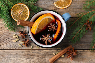 Tasty mulled wine in mug, spices and fir branches on wooden table, flat lay