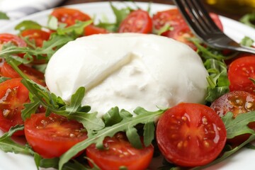 Delicious burrata cheese with arugula and tomatoes on plate, closeup