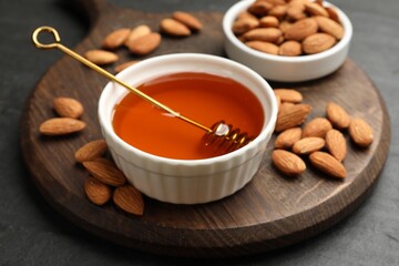 Delicious honey in bowl and almonds on dark textured table, closeup