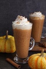 Delicious pumpkin latte with whipped cream, spices and fresh vegetables on dark textured table, closeup