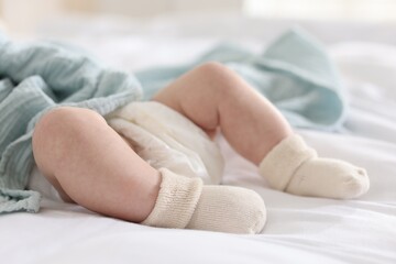 Cute newborn baby in diaper lying on bed indoors, closeup