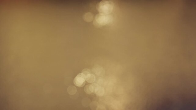 Dreamy 4K abstract footage of soft golden bokeh lights dancing and shimmering on perfectly calm water at sunset or golden hour. Warm, ethereal background for relaxation, wellness and meditation.