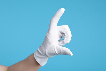 Woman in cloth glove showing size of something on light blue background, closeup
