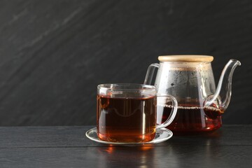 Hot tea in cup and teapot on black wooden table. Space for text
