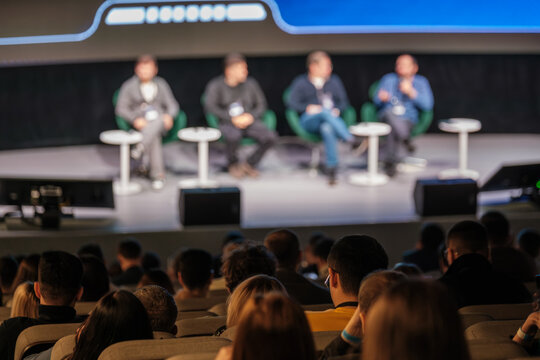 Panel discussion on stage with four speakers engaging audience during conference, capturing collaboration, learning, and networking in a large auditorium
