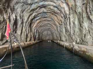 A boat glides through a historic Montenegrin submarine tunnel, its textured walls framing the...