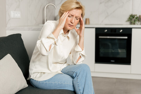 Woman experiencing severe headache at home while sitting on the couch