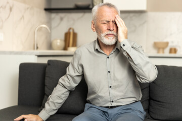 Elderly man suffering from headache in living room during daytime