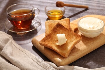 Fresh toasted bread slices with butter, honey and tea on grey table, closeup