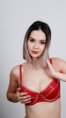 Obraz premium Confident woman in red lace bra and panties poses with hands up behind her head