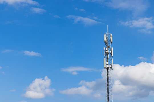 Tall telecommunications mast equipped with 5G and 4G and in the future 6G antennas against a bright blue sky with white clouds, symbolizing global digital connectivity. - Powered by Adobe