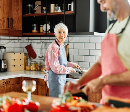 Portrait of happy senior mid aged mature couple prepering meal with fresh vegatebles in kitchen at hpme