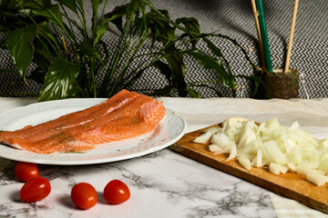 Salmon with fennel. A plate with a salmon fillet. On the table is also a cutting board with onions and cherry tomatoes.