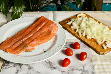 Salmon with fennel. A plate with a salmon fillet. On the table is also a cutting board with onions and cherry tomatoes.