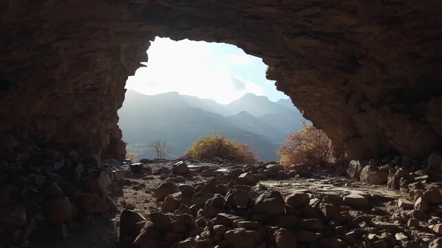 Sunlight illuminates the rocky path while exiting a dark cave with a scenic mountain view, Ansite fortress cave in Gran Canaria