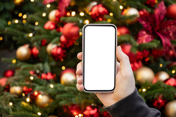 Smartphone with empty blank screen in mans hand against Christmas tree with light garland. Screen...