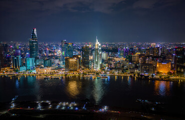Night aerial view of Ho Chi Minh City, Vietnam, with illuminated skyscrapers, riverside lights, and vibrant urban skyline reflecting on the water.