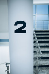 A clean, modern interior stairwell marked with a large number “2” on a white column, indicating...