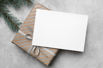 Blank Christmas or New Year greeting card mockup with copy space on top of a beautifully wrapped gift, surrounded by evergreen branches for festive ambiance