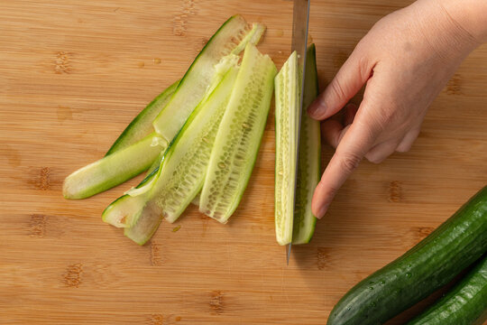 Slicing cucumbers with a large knife on wood cooking board close-up