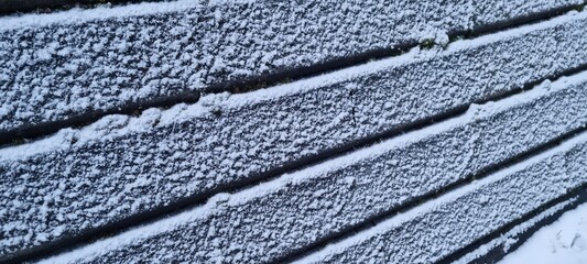 Snow covers a concrete wall creating patterns in a winter landscape near a rural area