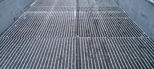 Grate surface in industrial setting showcases flooring design and open spaces for water drainage during daytime