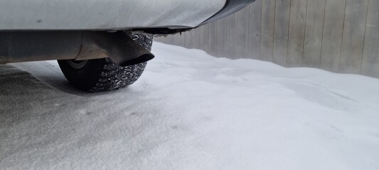 Snow-covered ground near a vehicle exhaust pipe with tire tracks from a recent drive in winter conditions