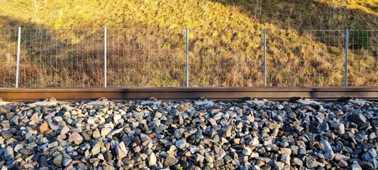 View of a railway track alongside a grassy slope with a fence during the early morning light