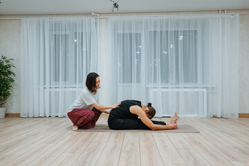 instructor offers support in peaceful yoga space emphasizing calm breathing, tranquil studio featuring instructor helping child stretch with soft lighting and wooden flooring