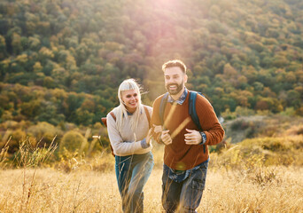 Hiking couple, young man and woman enjoys nature with trekking backpacks in a lush forest during a sunny day