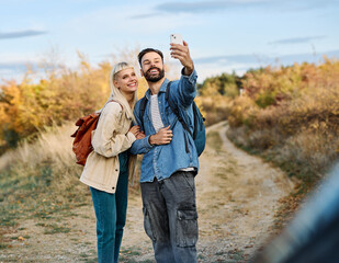 Hiking couple enjoys nature  and takes a selfie photo with a mobile phone  in a lush forest during a sunny day
