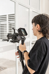 Primer plano de joven con c&aacute;mara en mano y monitor digital filmando secuencia en industria, vertical
