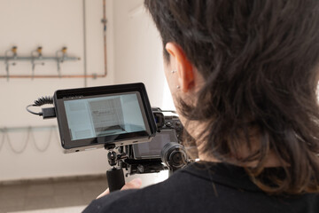 Primer plano de joven con cámara en mano y monitor digital filmando secuencia en fábrica	
