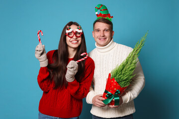 Happy couple with Christmas accessories, thuja tree and candy canes on light blue background