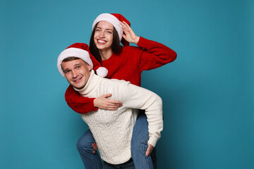 Fototapeta premium Smiling couple in Santa hats having fun on light blue background. Merry Christmas and Happy New Year
